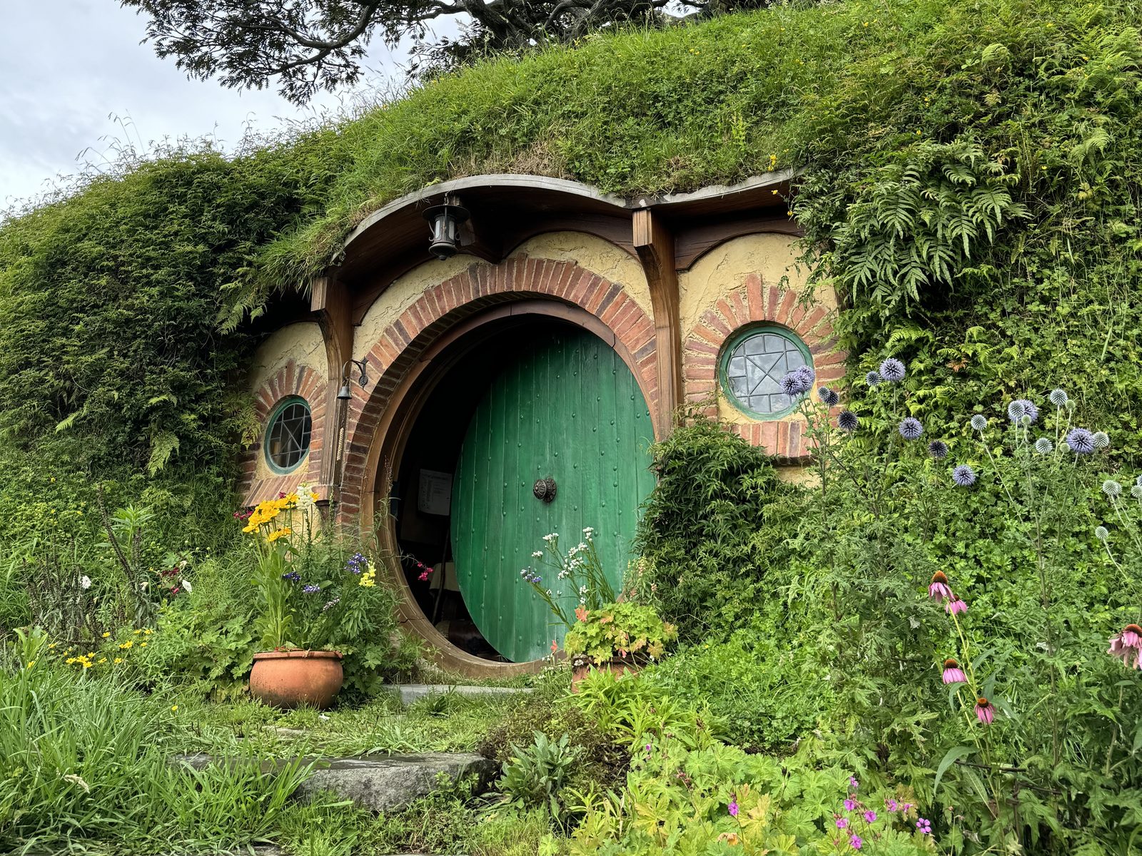 Puerta verde de una casa hobbit entre flores, en Hobbiton