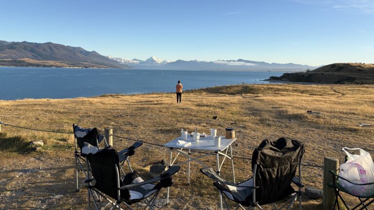 Mesa y sillas de camping frente a un lago con montañas nevadas