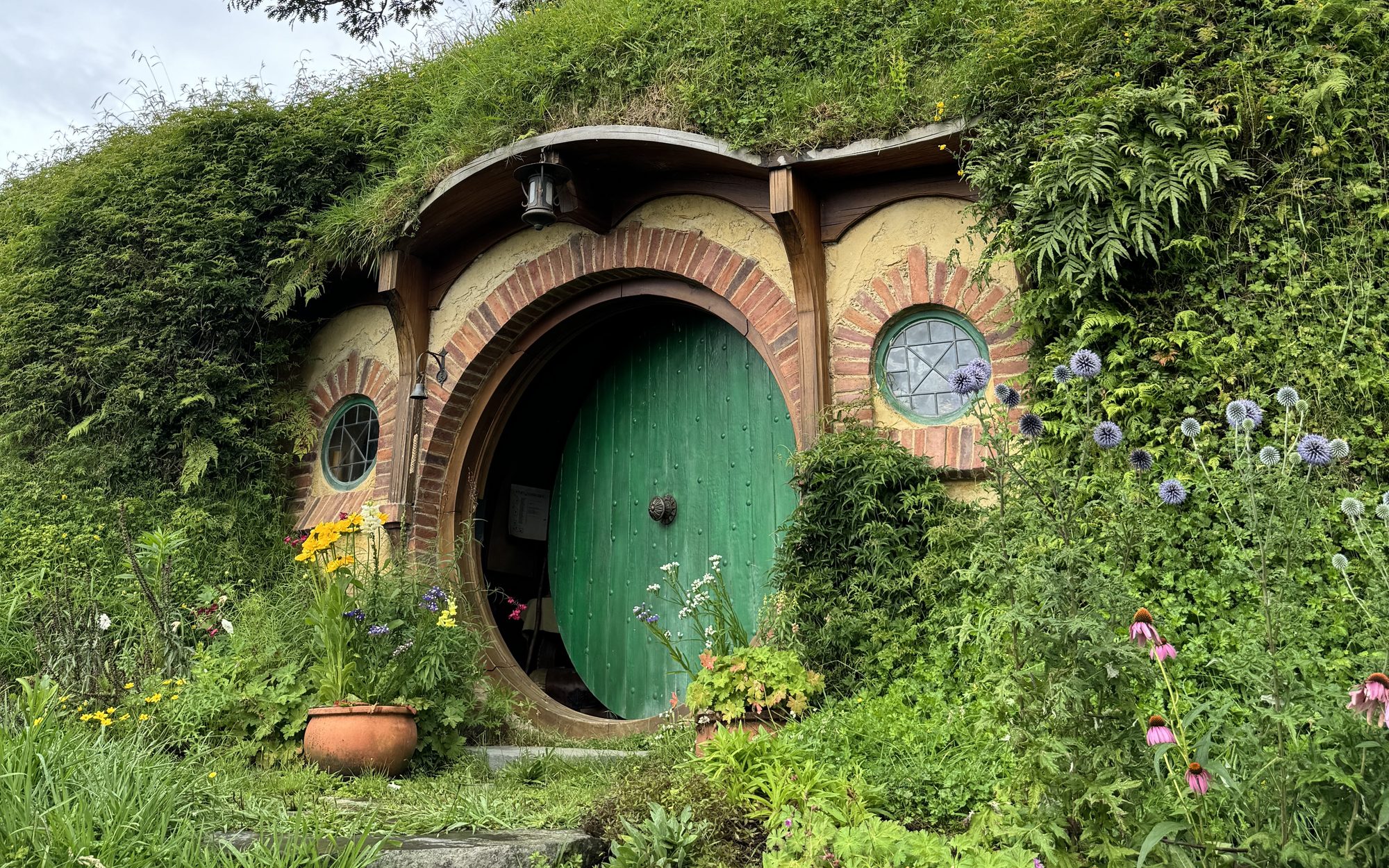 Puerta verde de una casa hobbit entre flores, en Hobbiton